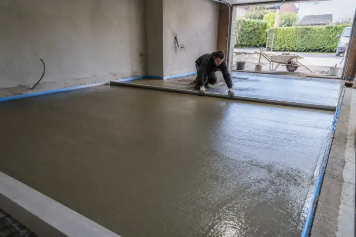 Pracownik wyrównuje świeży beton, tworząc połączenie posadzki garażu z podjazdem.